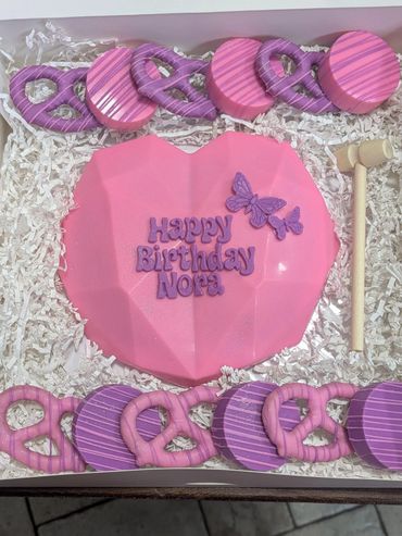 Pink heart-shaped cake with purple lettering and butterfly decoration for Nora's birthday.