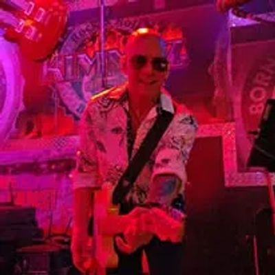 Musician playing guitar on stage bathed in red light.