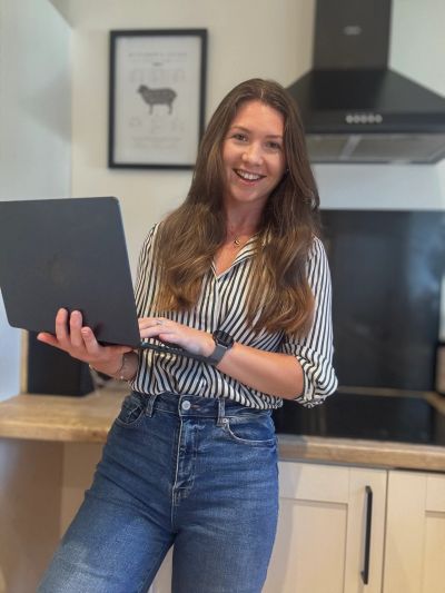 A woman holding a laptop and smiling in a kitchen.