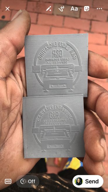 Hand holding two gray laser-engraved plates with company logos.