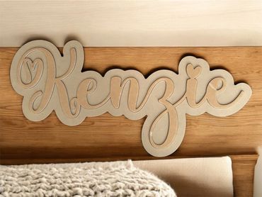 Wooden name sign reading 'Kenzie' on a wooden surface.