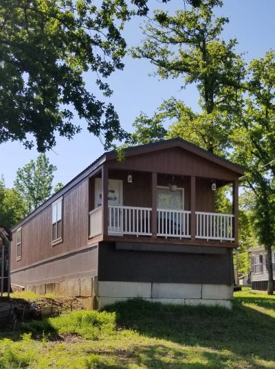 A brown mobile home with a small front porch surrounded by trees.