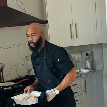 Bearded man in a black apron preparing food in a modern kitchen.
