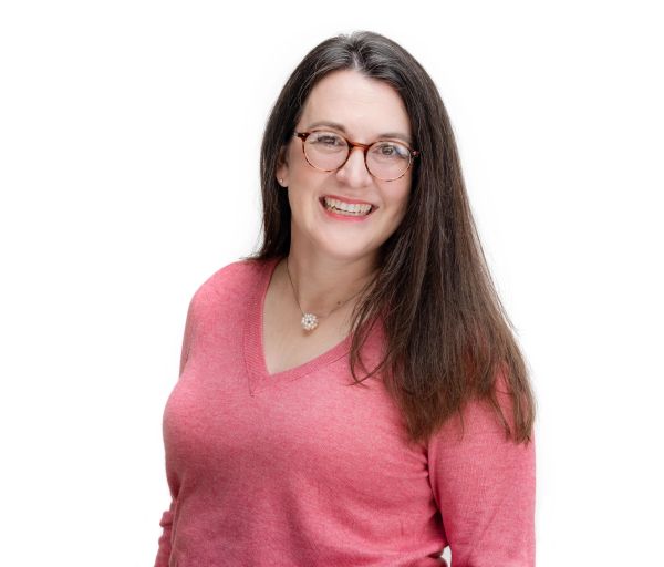 Smiling woman with glasses and long hair in a pink sweater.