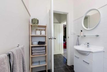 Minimalist bathroom with white walls, wooden shelf, and round mirror.
