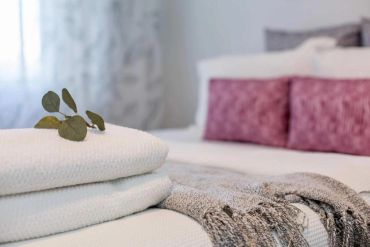 Neatly folded white towels with a green leaf on a bed with pink cushions.