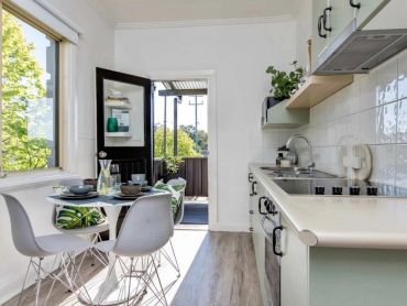Bright kitchen with dining table and outdoor access, featuring modern white chairs and leafy decor.