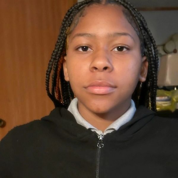 Young person with braided hair wearing a black zip-up hoodie.