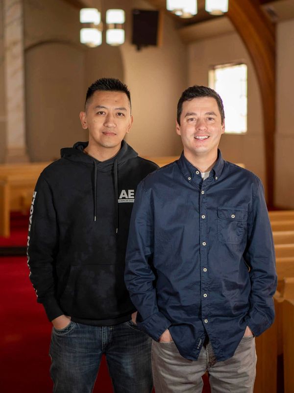 Two men standing inside a church with hands in pockets.