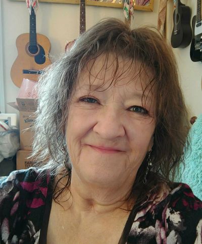 Smiling woman with guitars in the background.