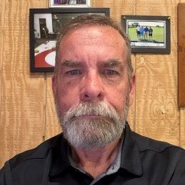 Portrait of a bearded man in front of wood-paneled wall.