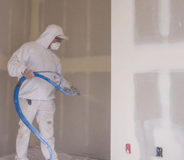 Worker spray-painting an interior wall while wearing protective gear.