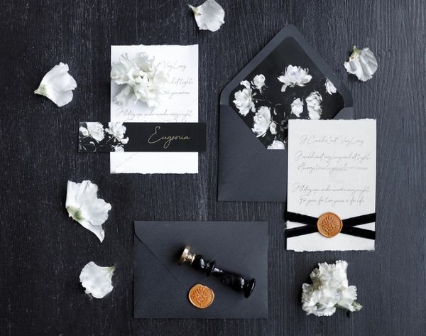 Elegant black and white floral wedding invitations with wax seals and flower petals.
