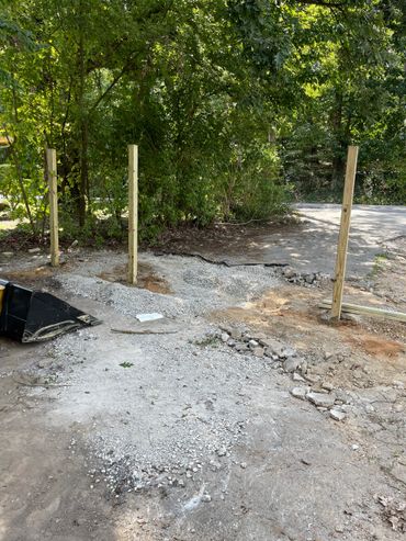 Three wooden posts installed in a gravel-filled outdoor area near trees.