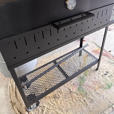 A black outdoor grill with a temperature gauge and mesh lower shelf.