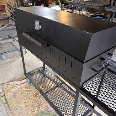 A black metal smoker grill with a temperature gauge in a workshop.
