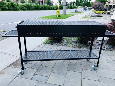 Black metal grill on wheels with side shelves on a patio.