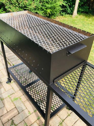 Large black metal barbecue grill on a patio with grass and bushes in the background.