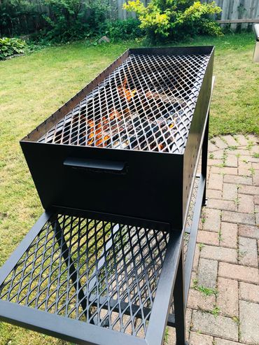 Black metal grill with fire burning inside, set in a backyard.