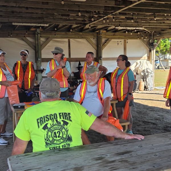 Group of people wearing safety vests under a pavilion.