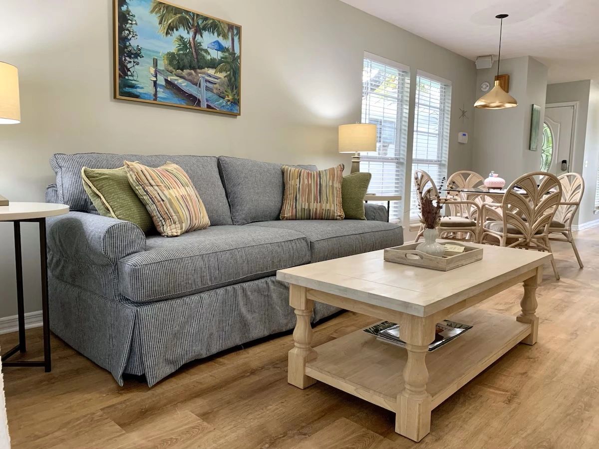Cozy living room with a striped gray sofa, wooden coffee table, and dining area with rattan chairs.