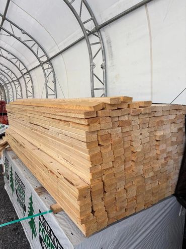Stacked smooth wooden boards on a wrapped pallet, secured with a green strap outdoors.