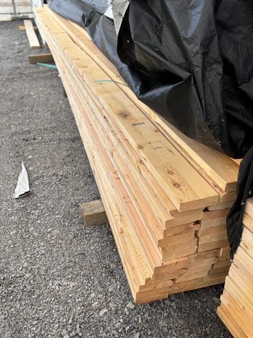 Neatly stacked wooden planks with a black tarp partially covering the top.