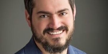Smiling man with beard in a blue suit jacket.