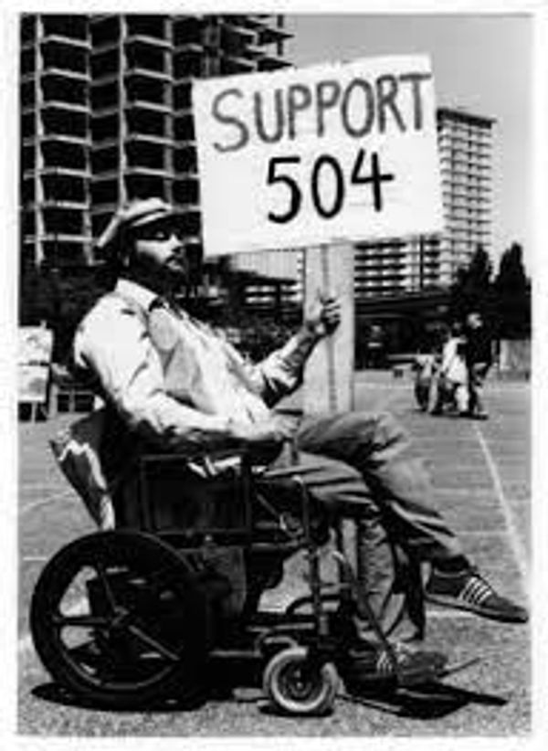 old black and white photo of man in wheelchair holding sign that says support 504