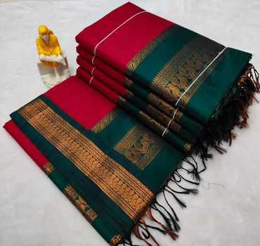 Stack of red and green sarees with golden embroidery and a small yellow figurine.