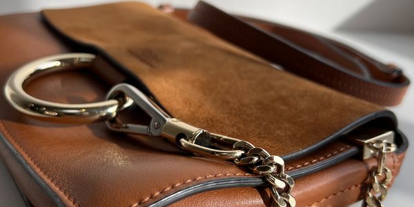Close-up of a stylish brown leather handbag with gold chain details.