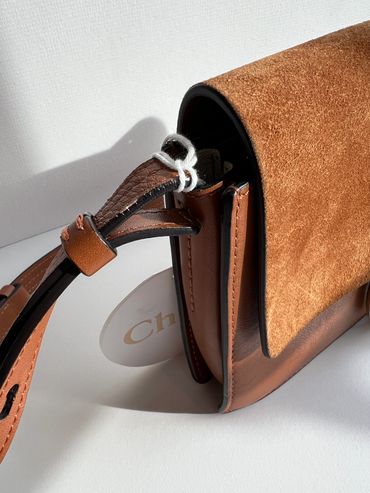 Close-up of a brown suede and leather handbag with a stitched strap.