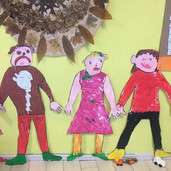 Disegni di persone con foglie secche appese al muro.