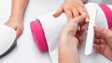 A hand receiving a manicure with a nail file over a white towel and pink cushion.