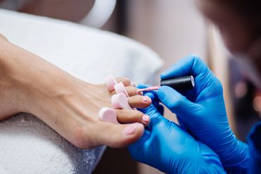 Close-up of a pedicure with pink nail polish being applied to toenails.
