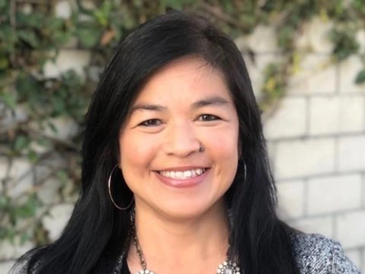 Smiling woman with long black hair and hoop earrings.