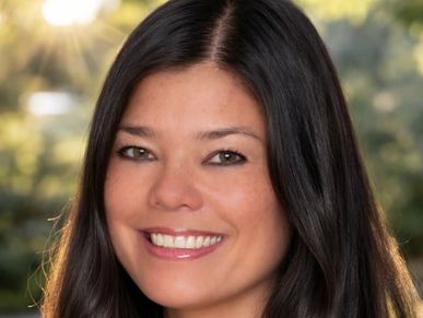 Smiling woman with long dark hair outdoors.