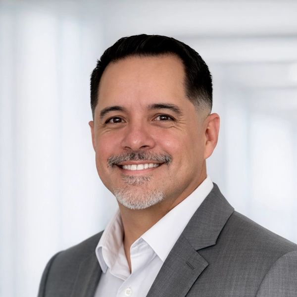 Professional man in gray suit smiling against a bright background.