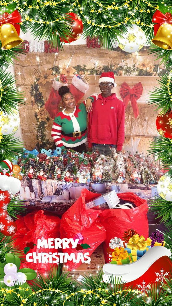 Two people smiling behind a table full of Christmas gift bags and decorations.