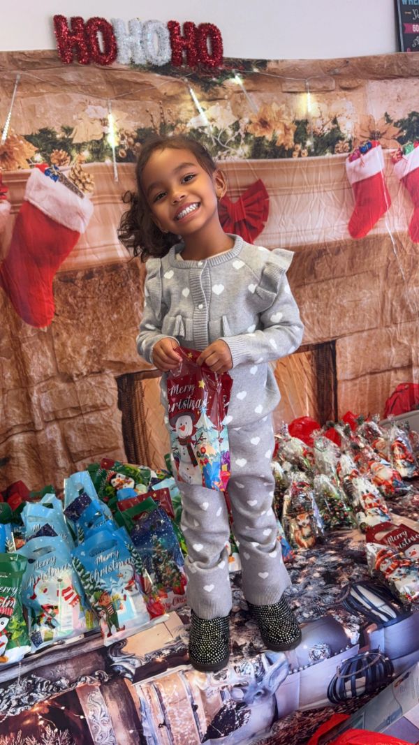 Smiling girl in heart-patterned pajamas with Christmas gifts.