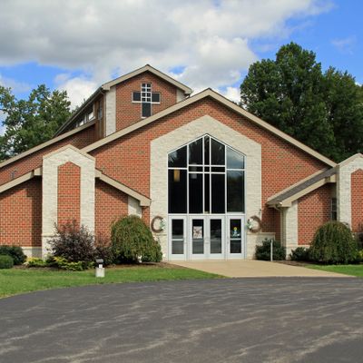 A brick church building with large windows and a cross under a partly cloudy sky.