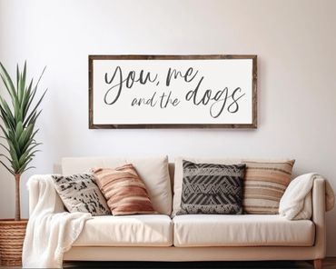 Cozy living room with a sofa, patterned pillows, a plant, and a framed quote about dogs.