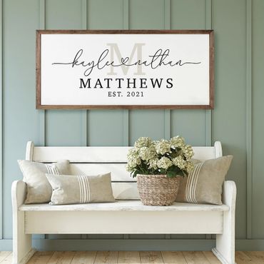 Rustic white bench with cushions and floral basket under a personalized family name sign.