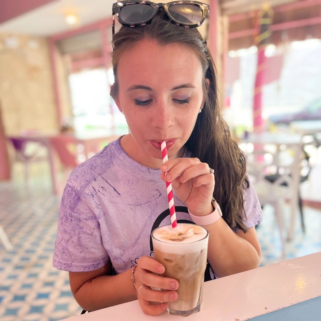 Woman enjoying a creamy iced coffee with a striped straw indoors.