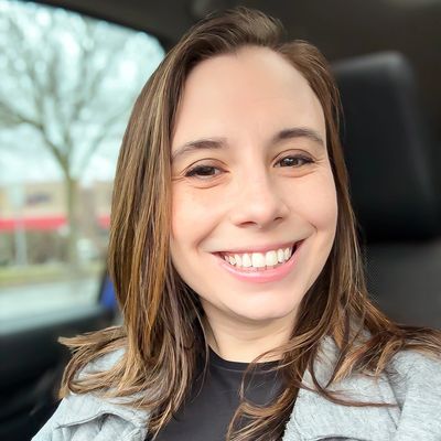 A smiling woman with brown hair inside a car.