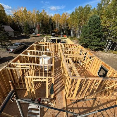 Wooden framework of a house under construction in a forested area.
