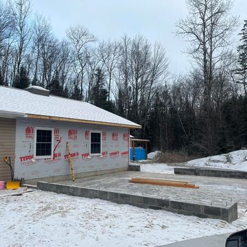 Construction site with a house and a concrete foundation in snowy weather.