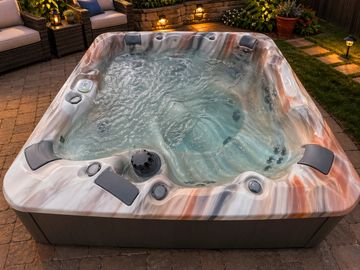 A filled outdoor hot tub with jets and headrests on a patio at night.