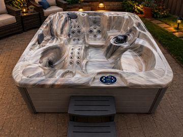 Modern outdoor hot tub with multiple jets and seating areas on a patio.