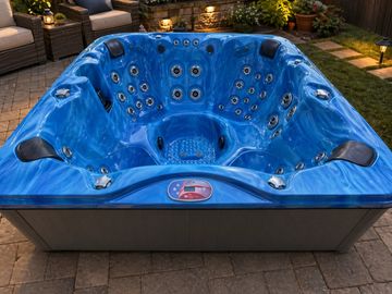 Empty blue hot tub with multiple jets on a patio at dusk.